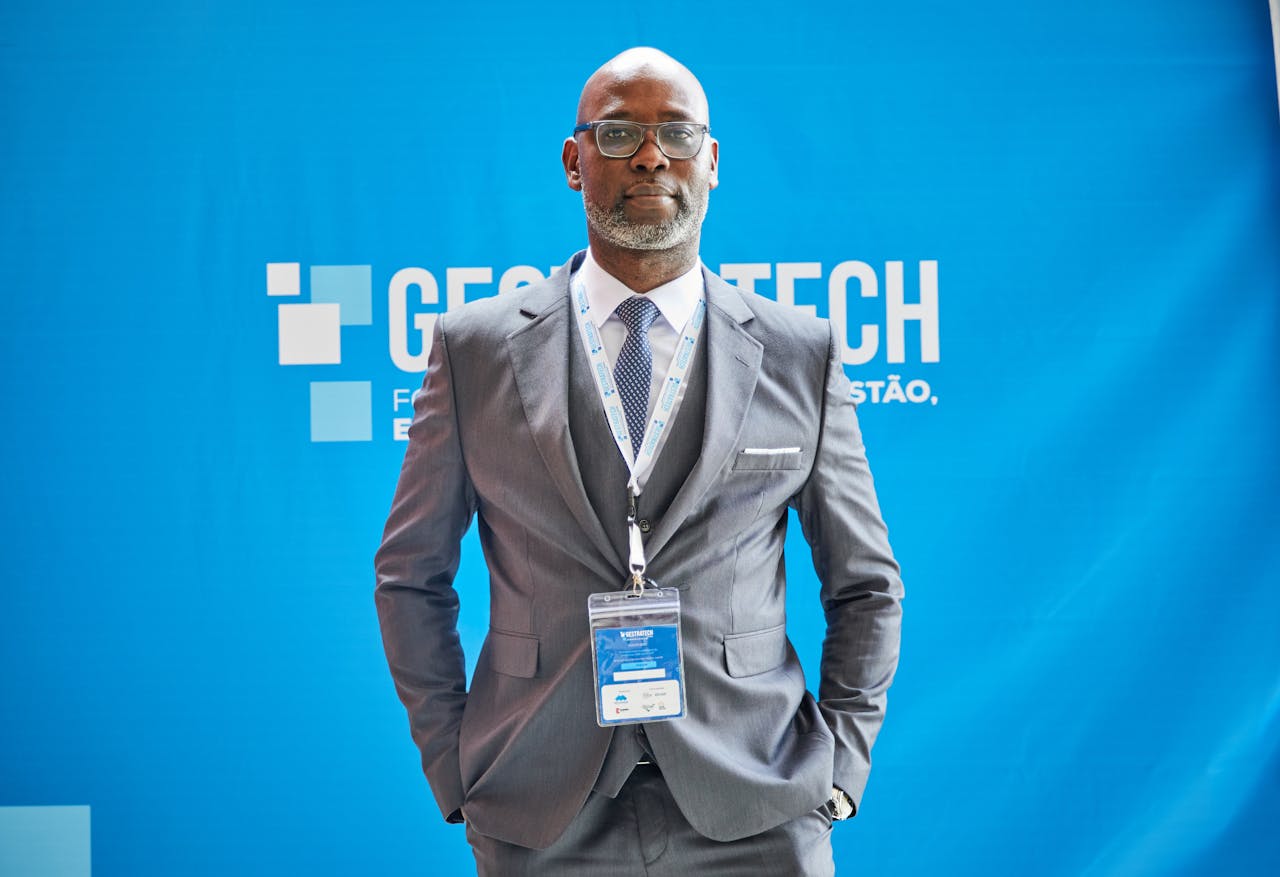 Confident African man in a grey suit at a trade fair with blue photo wall backdrop.